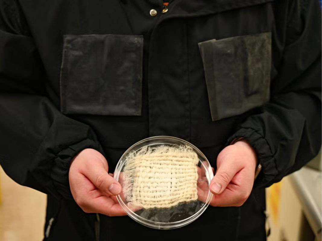Researcher wears a black jacket in a lab while holding a beige-colored woven textile