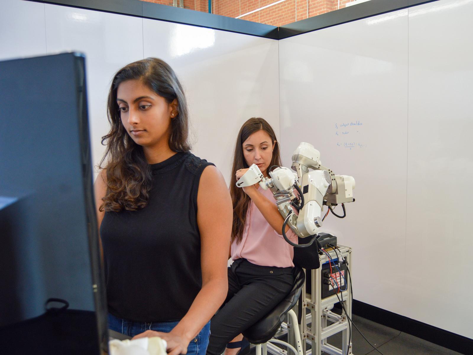 two students looking at and holding robot arm