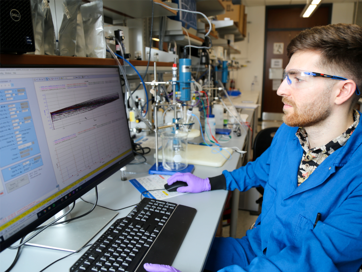 Texas Engineering researcher wearing lab safety gear typing at computer monitor.