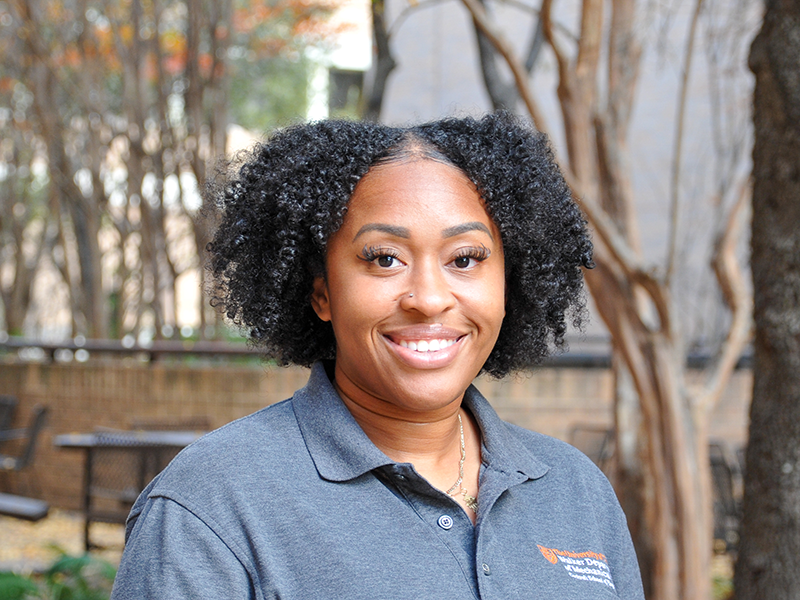 Shante Tyus smiling outside surrounded by trees on UT Austin campus.