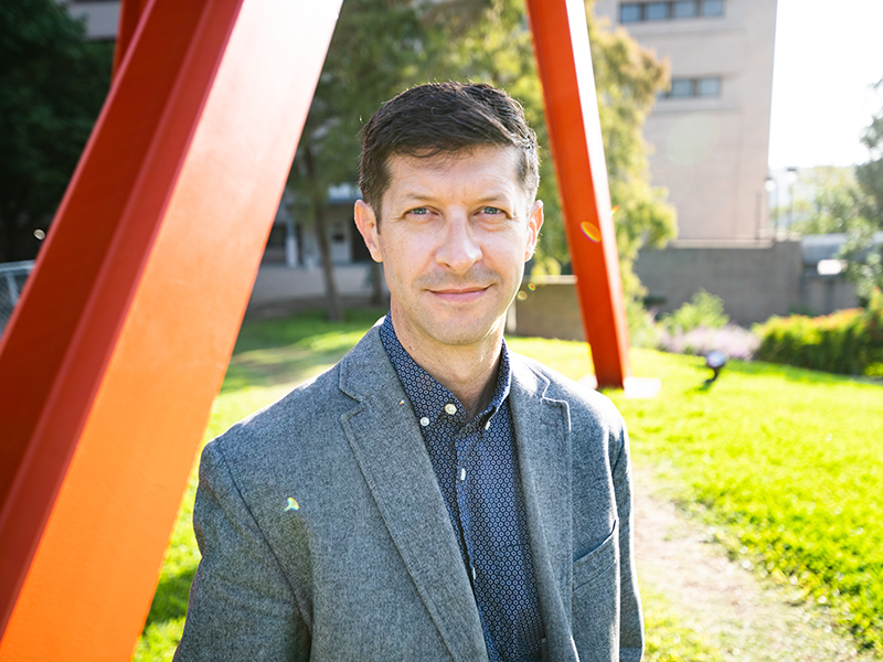 Michael Haberman smiling in front of Clock Knot sculpture on UT Austin campus.