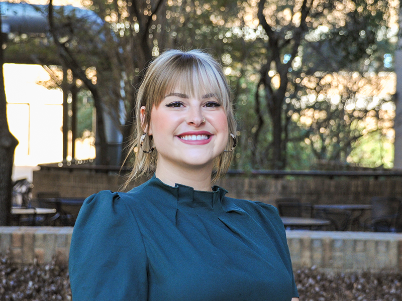 Christina Lambott smiling surrounded by trees on UT Austin campus.