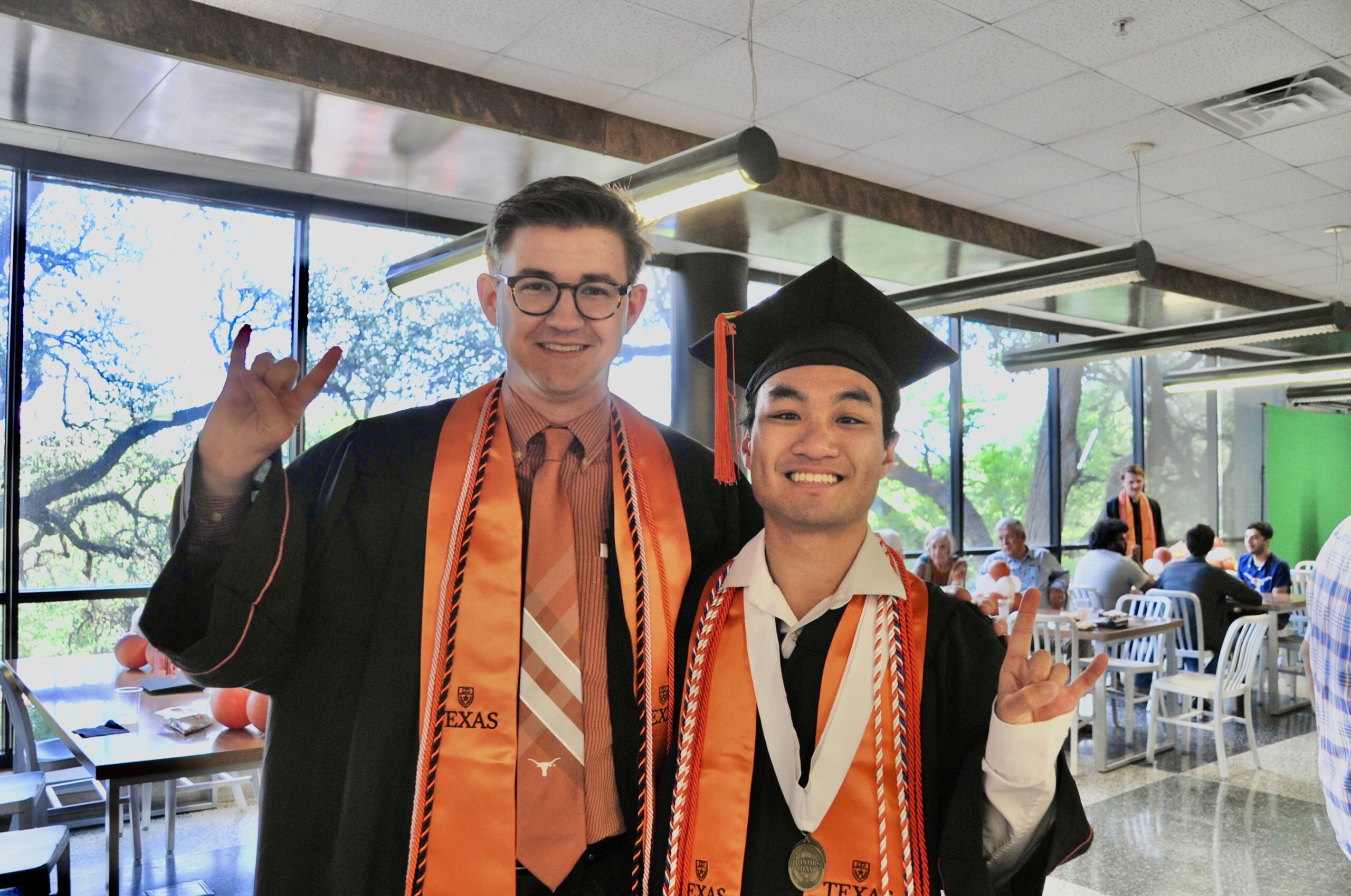 UT Mechanical Engineering students in graduation cap and gown throwing a Hook 'Em